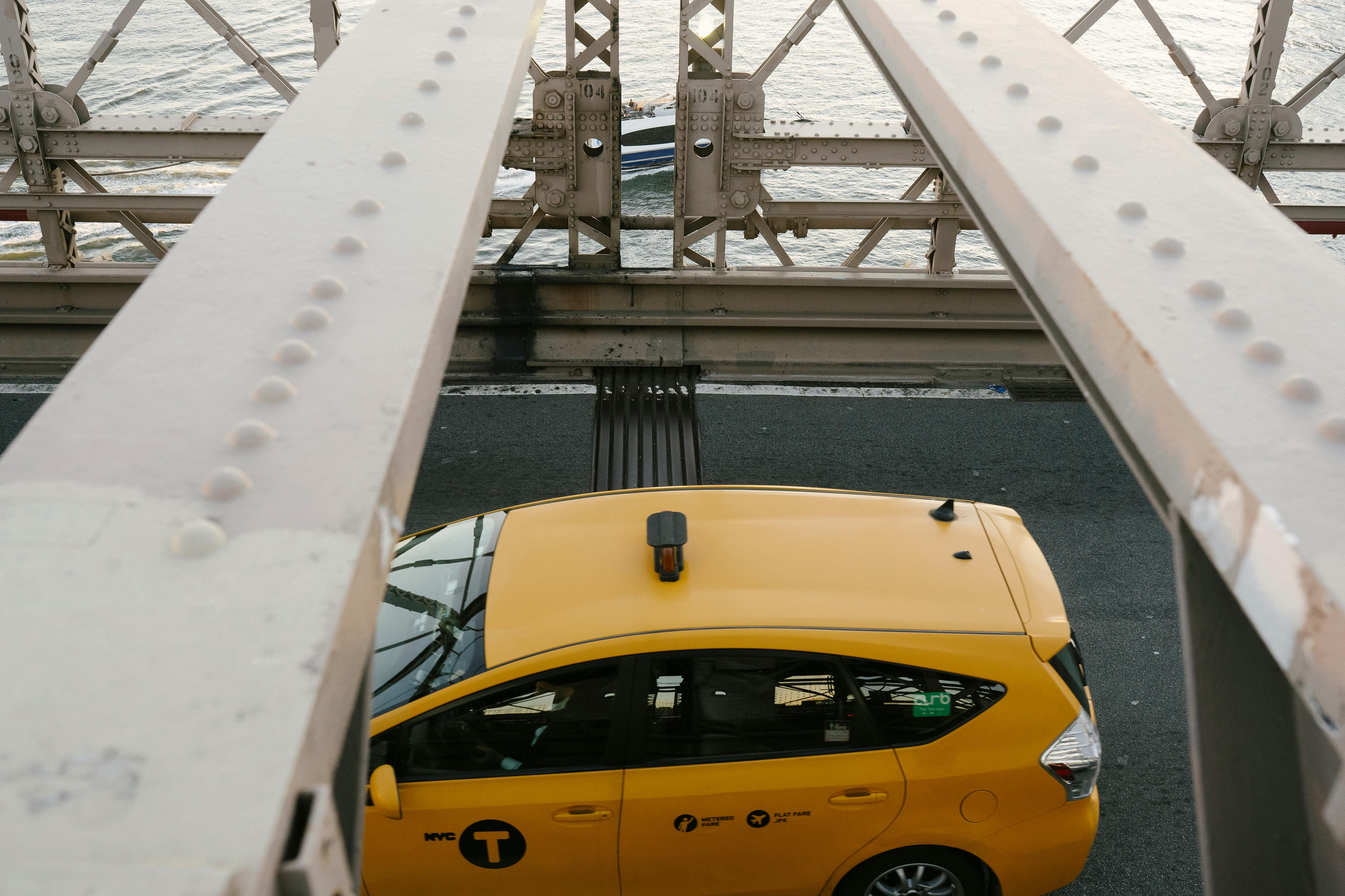 yellow cab driving on metal bridge