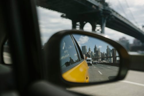 Side mirror reflecting city and road while driving on modern with city skyscrapers on background