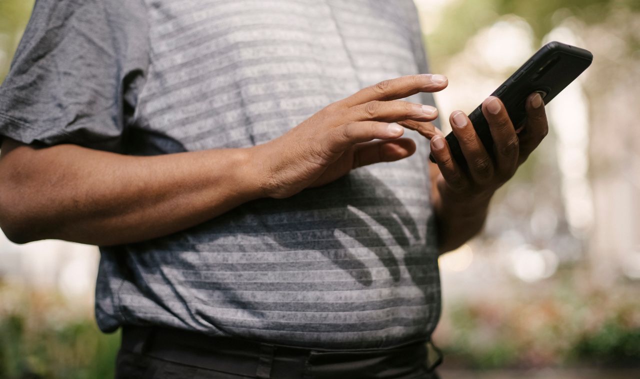 crop anonymous male in casual clothes using smartphone on blurred back