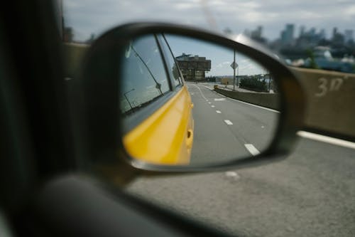 Side mirror of car reflecting road with marks and building on sunny day