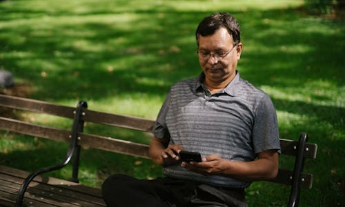 Ethnic male in casual outfit using smartphone while sitting on bench on park