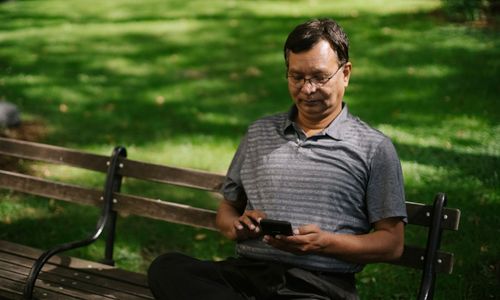 Free Ethnic male in casual outfit using smartphone while sitting on bench on park Stock Photo