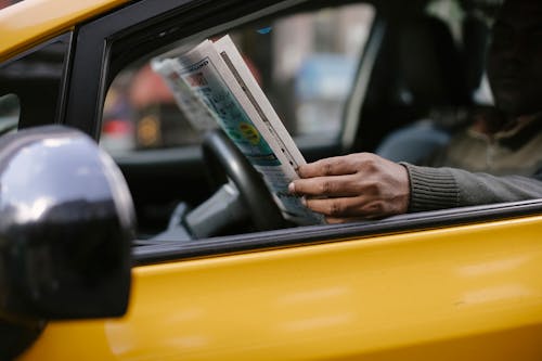 Side view of crop anonymous ethnc male driver reading information in newspaper article while waiting for client