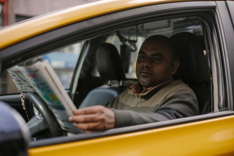 Serious Ethnic Male Taxi Driver Reading Newspaper