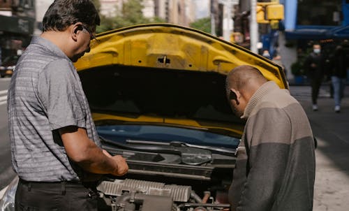 Ethnic mechanic checking car standing near man