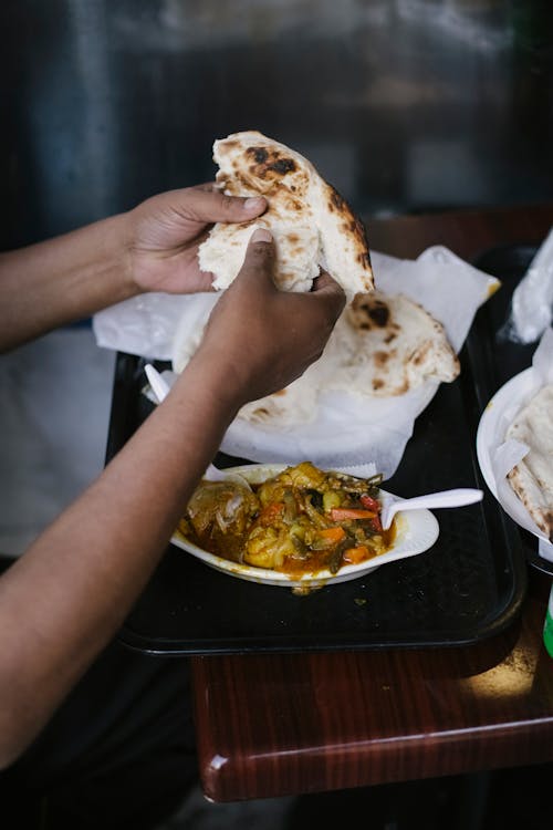 Free High angle of crop faceless ethnic male eating curry with roti bread at table in cafe Stock Photo