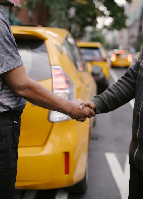 Free Side view of crop faceless ethnic males having handshake concluding agreement standing on road near taxi Stock Photo