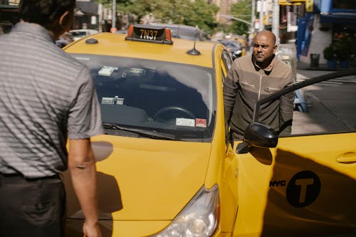 Free Serious ethnic cab driver having conversation with man in sunny day in New York Stock Photo