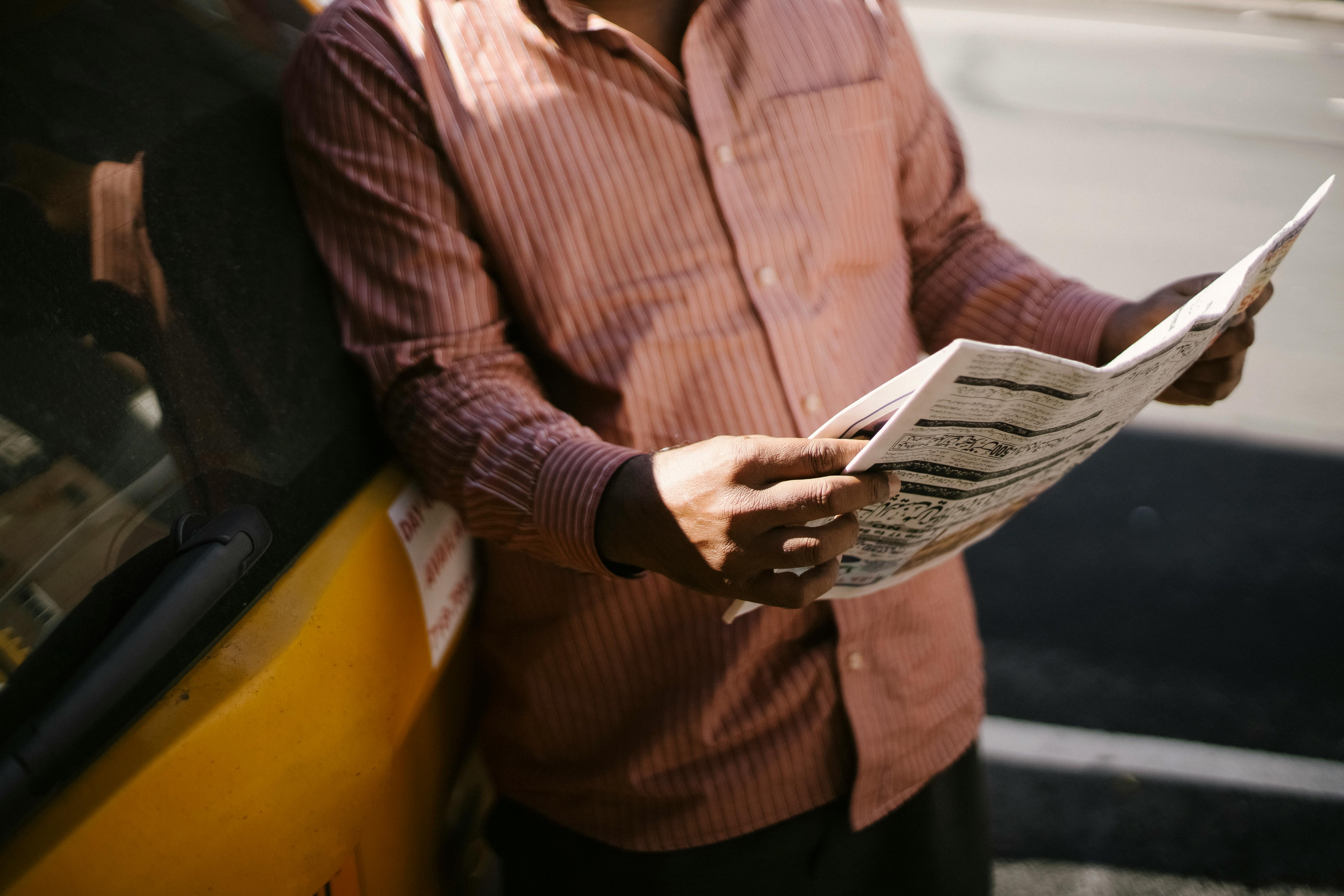crop ethnic male taxi driver reading newspaper in town