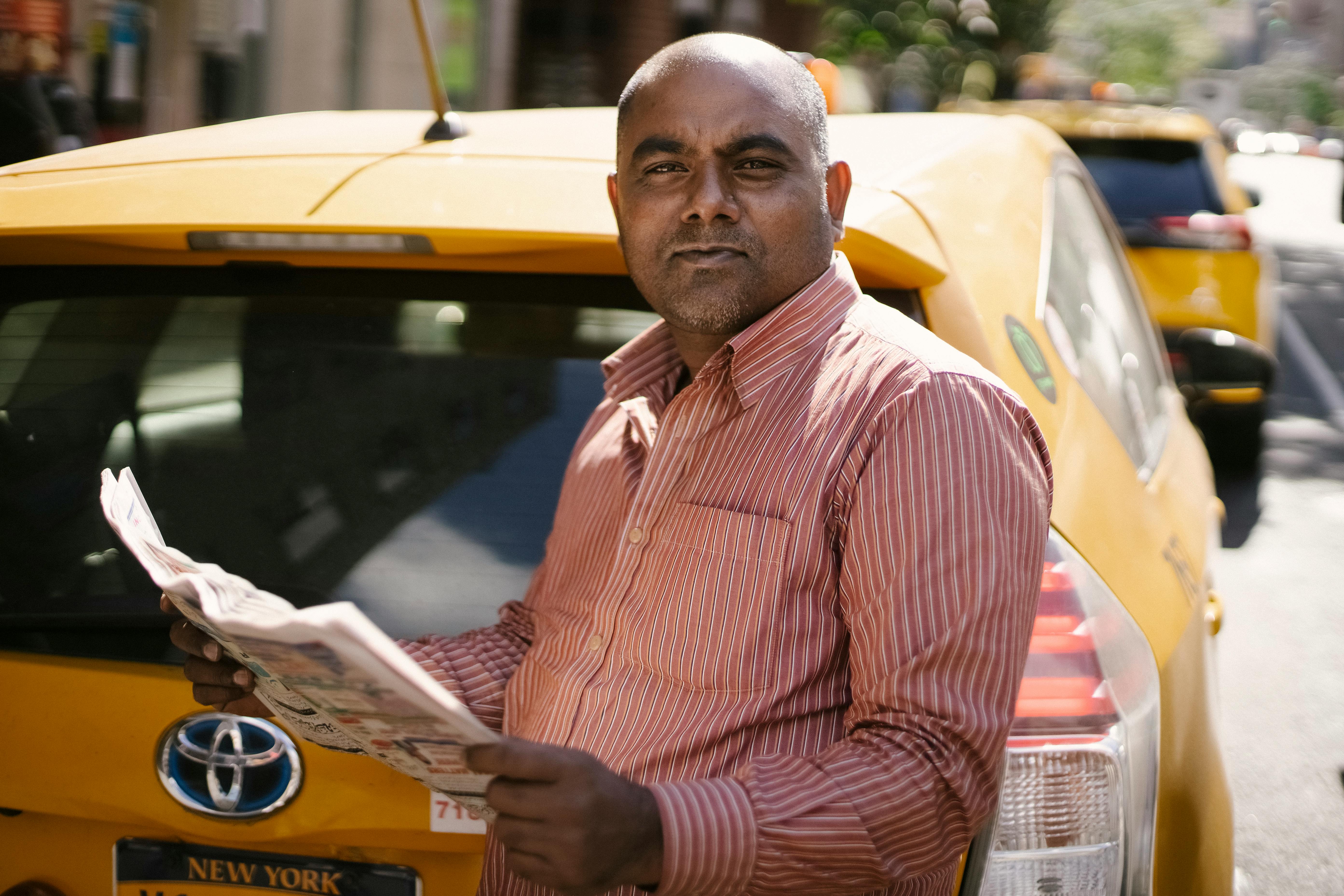 ethnic male cab driver with newspaper near vehicle in town
