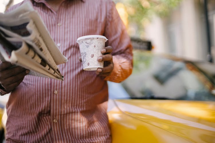 Crop Ethnic Taxi Driver With Takeaway Coffee And Newspaper