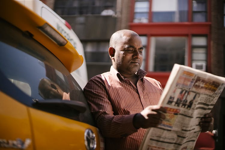 Interested Ethnic Cab Driver Reading Newspaper On Street