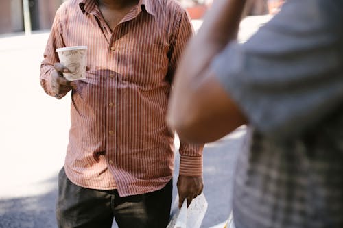 Faceless ethnic friends with takeaway coffee interacting on urban roadway