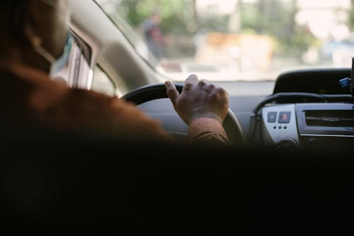 Crop ethnic man driving vehicle in town