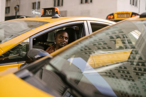 Этнический водитель такси отдыхает в современном желтом автомобиле в городе