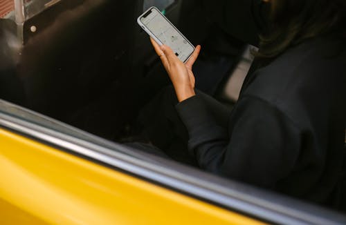 Crop passenger with navigator app on smartphone in taxi vehicle