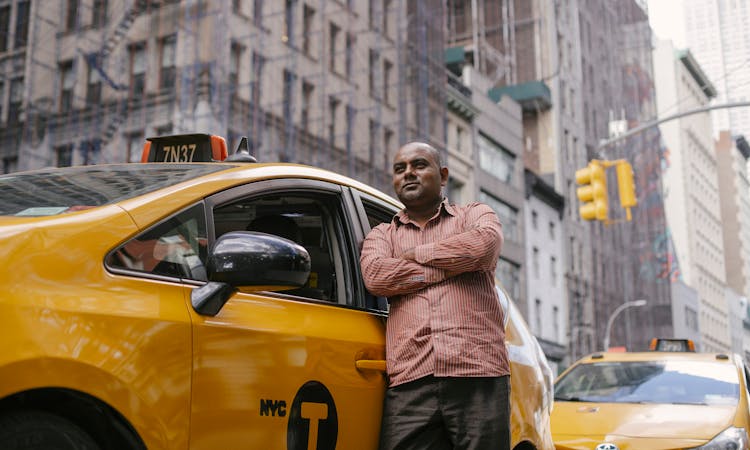 Self Confident Ethnic Taxi Driver Leaning On Car In City