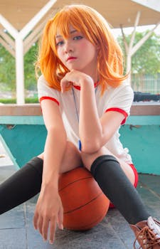 A young woman in cosplay with orange hair poses intricately with a basketball outdoors.
