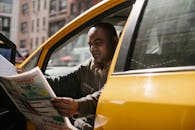 Concentrated male driver in casual clothes sitting in taxi during break and reading newspaper