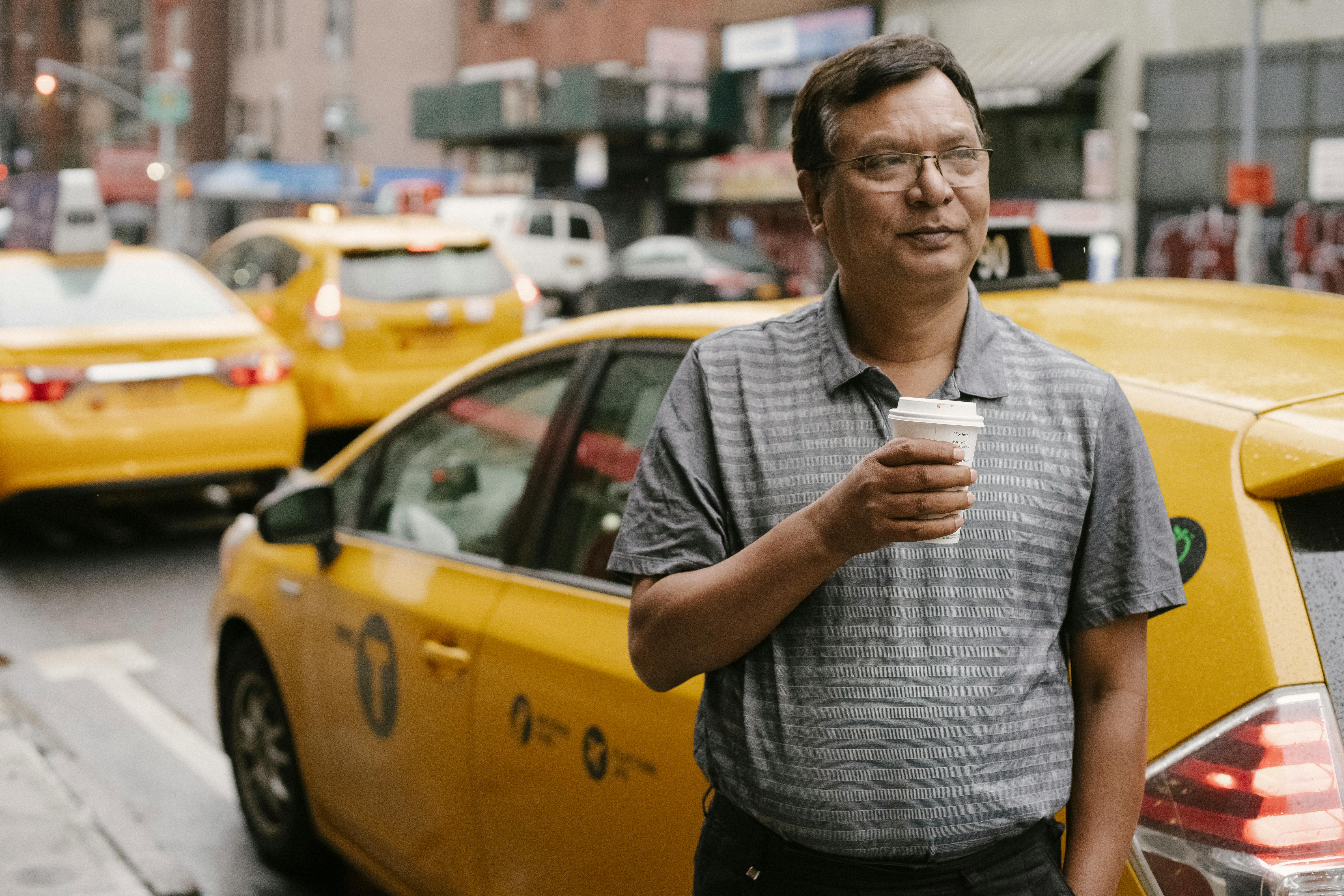 man drinking coffee against taxi on street