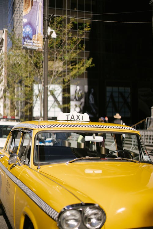 Yellow taxi with vintage design and yellow color on roadside of modern city street