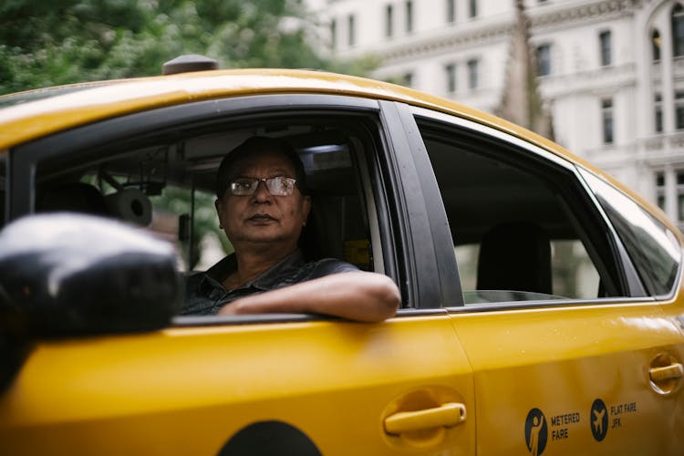 Ethnic Man Driving Taxi On City Street