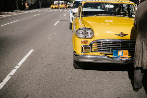 Free Back view of crop faceless driver standing near vintage yellow colored cab with chrome details on asphalt road of city Stock Photo
