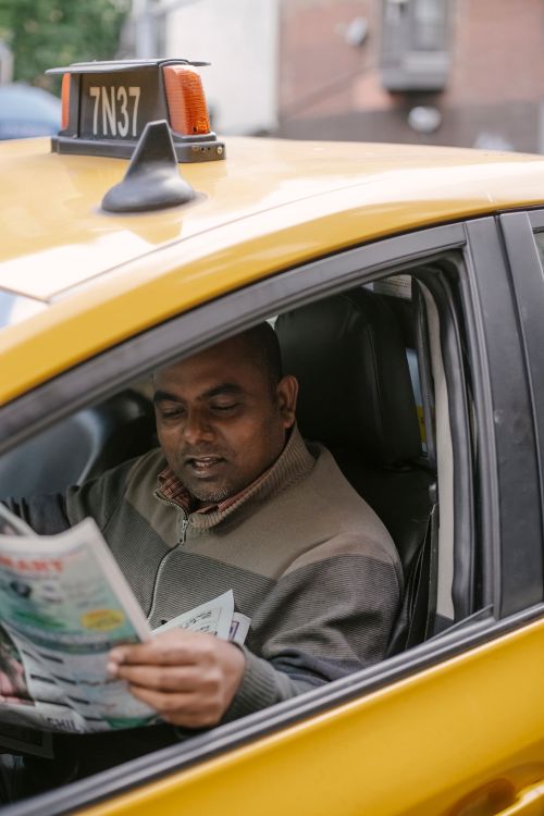 Free Ethnic male driver sitting in cab on city street while waiting passenger and reading newspaper Stock Photo