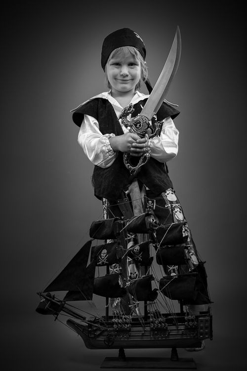 Free A young child dressed as a pirate with a toy ship and sword, smiling confidently. Stock Photo