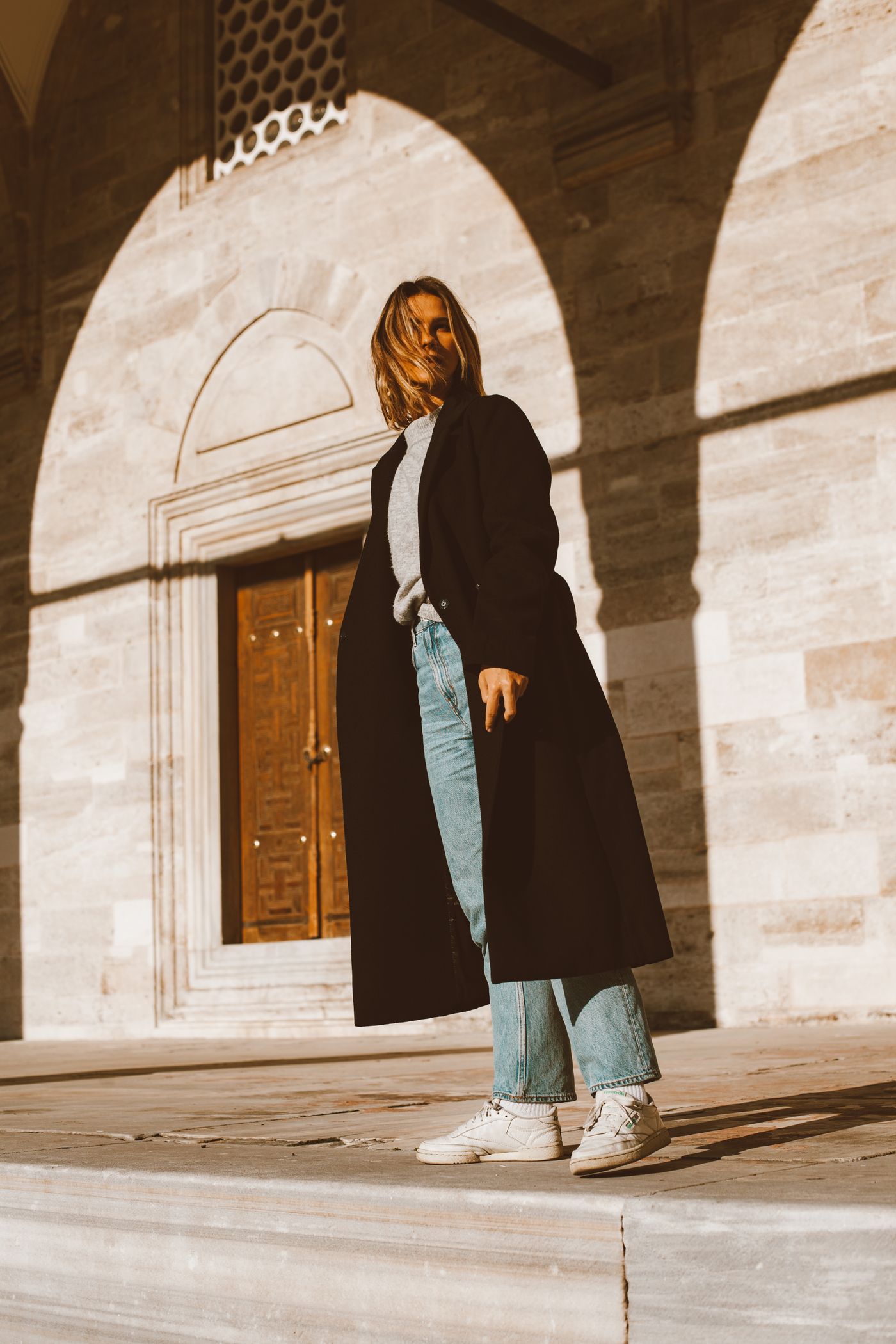 A woman in a black trench coat and denim pants — the off-duty CBK formula