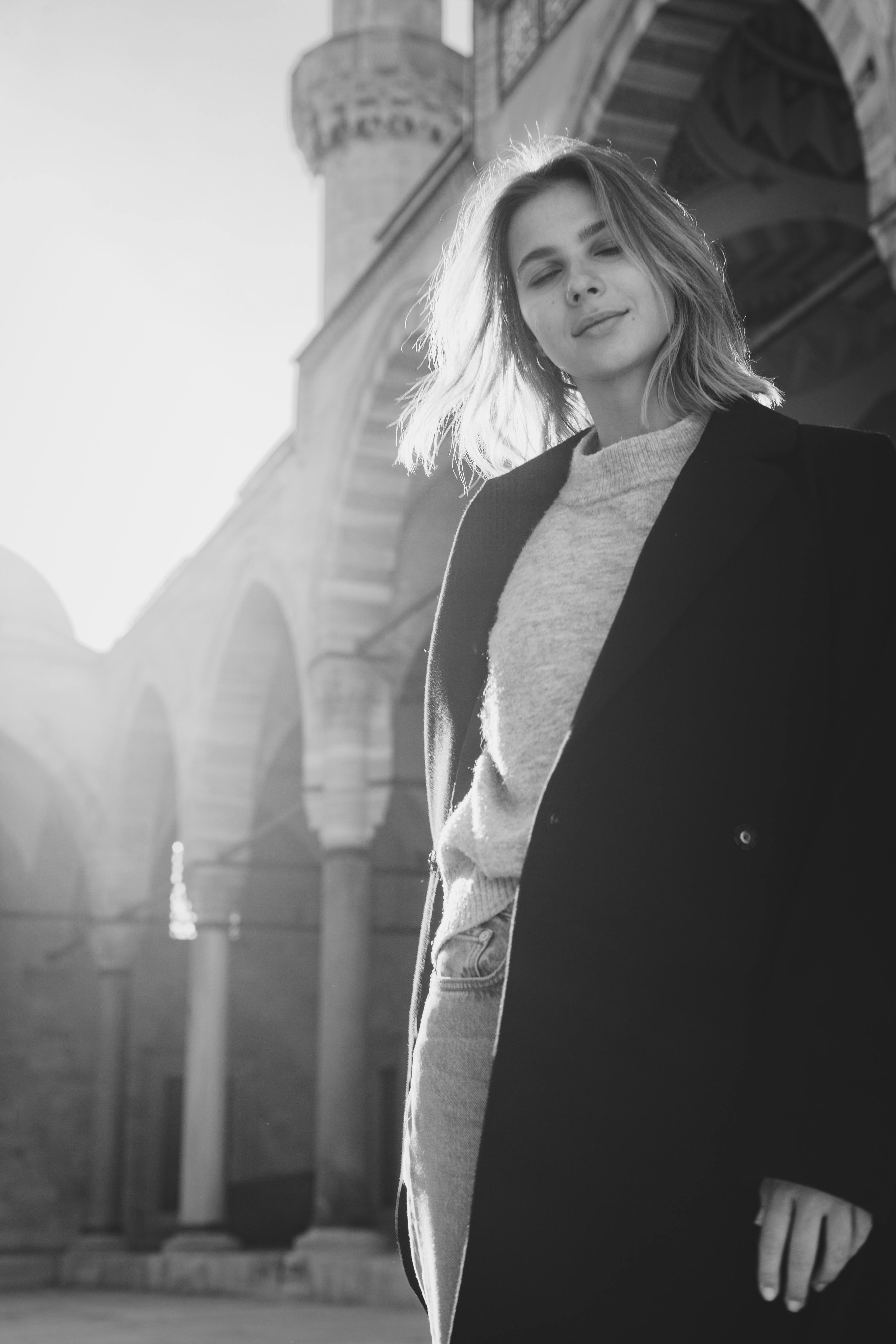 woman in black coat standing near columns