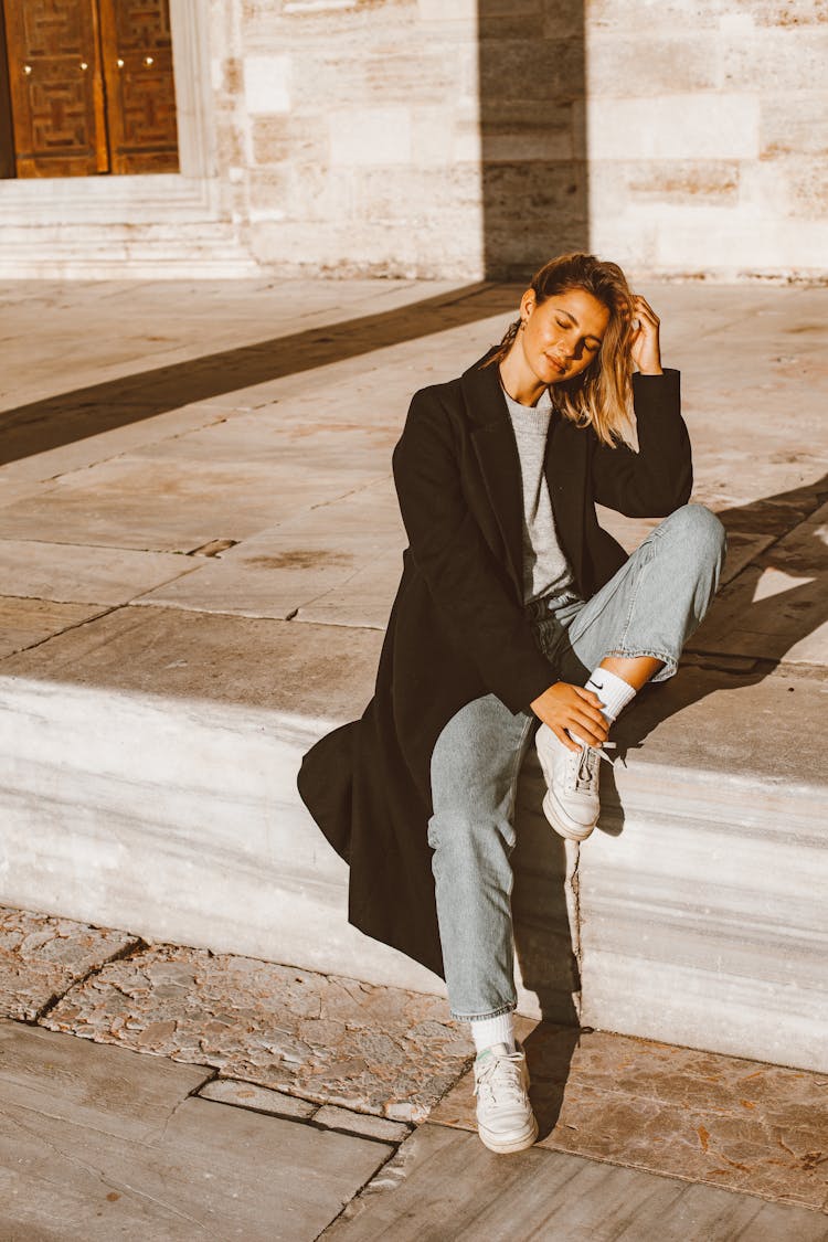 Woman In Black Coat Sitting On Concrete Floor