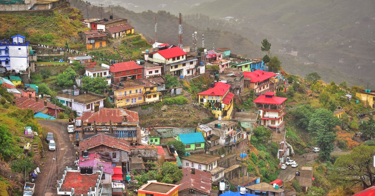 A vibrant aerial view of a colorful hillside town in Shimla with misty mountains.