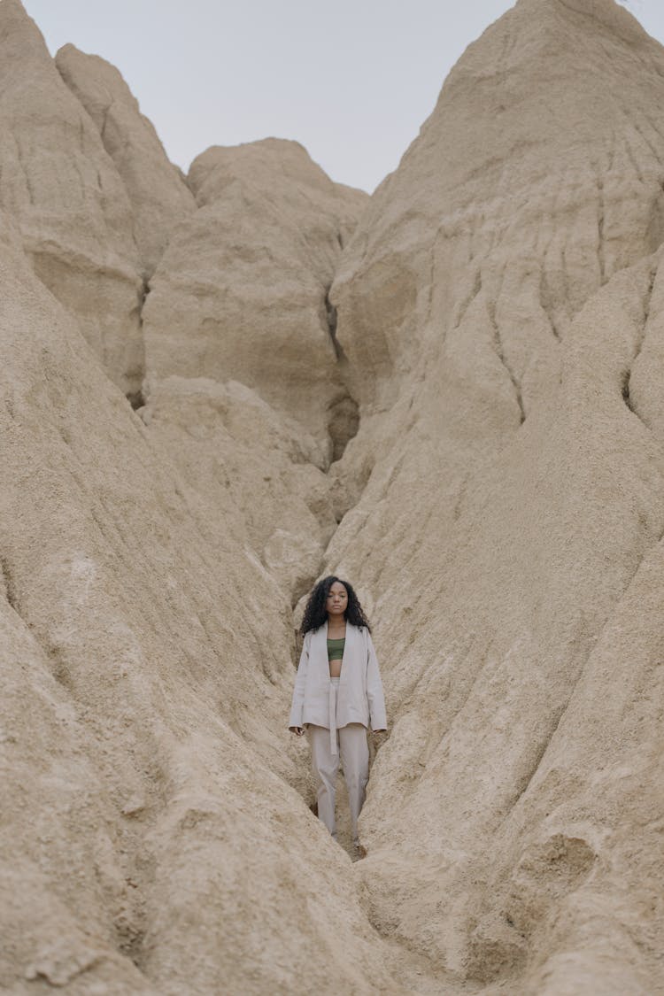 Woman In White Jacket Standing On Brown Rock Formation