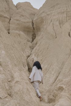 Woman in white apparel walking through a narrow sandy desert canyon.