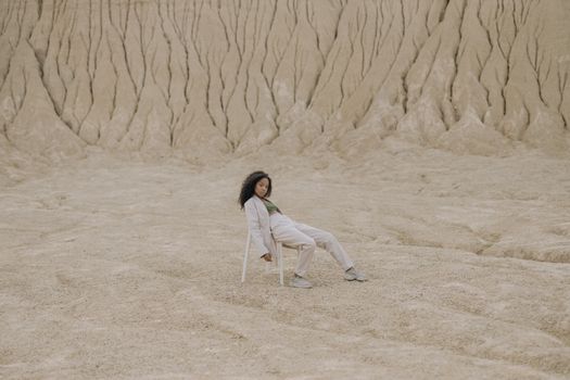 一名妇女穿着白色衣服，在干燥的沙漠荒地上放松地坐在椅子上