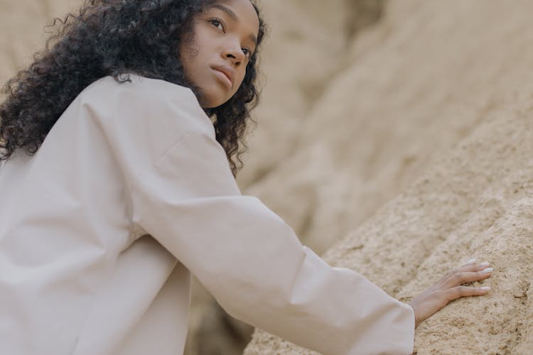 Woman In White Long Sleeve Shirt With Hand On Brown Rough Surface