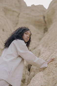 一名卷发女子穿着浅色衬衫，在户外探索岩石地形