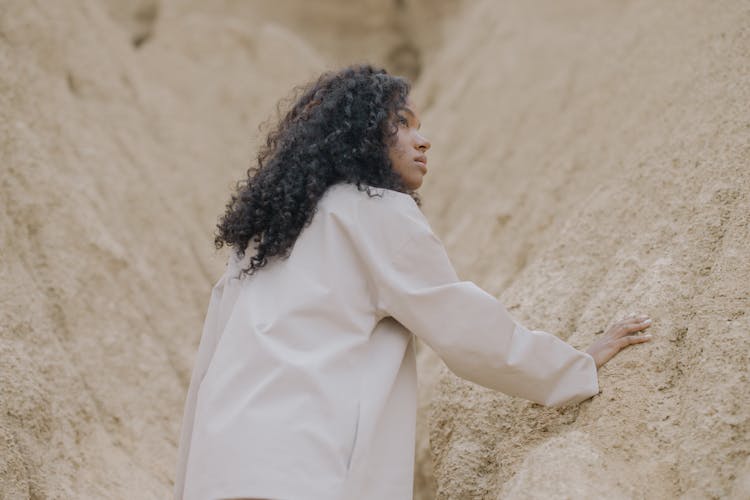 Woman In White Long Sleeve Shirt With Hand On Brown Rough Surface