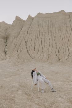 一名妇女坐在沙漠中干燥的椅子上，周围是受侵蚀的地层