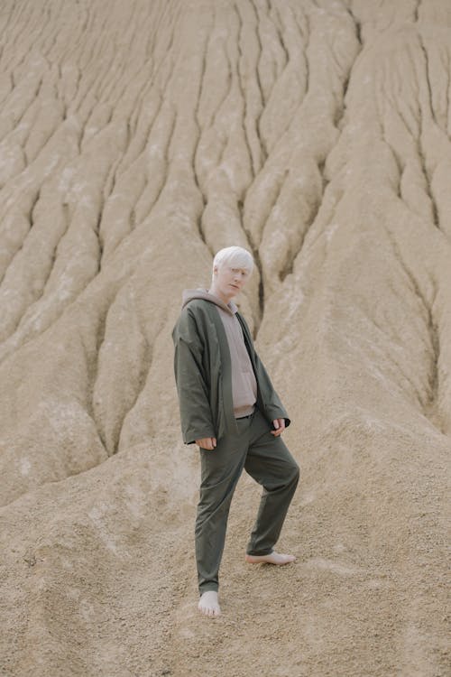Man in Gray Terno Standing on Slope of Brown Sand