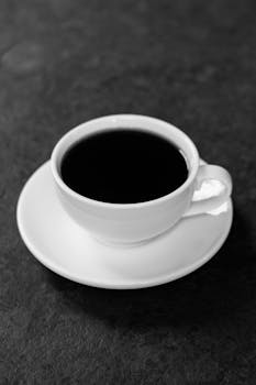 Black coffee in a white cup on saucer against a dark background, studio shot.