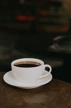 一杯热气腾腾的咖啡装在白色杯子和托盘里，放在深色背景的乡村桌子上