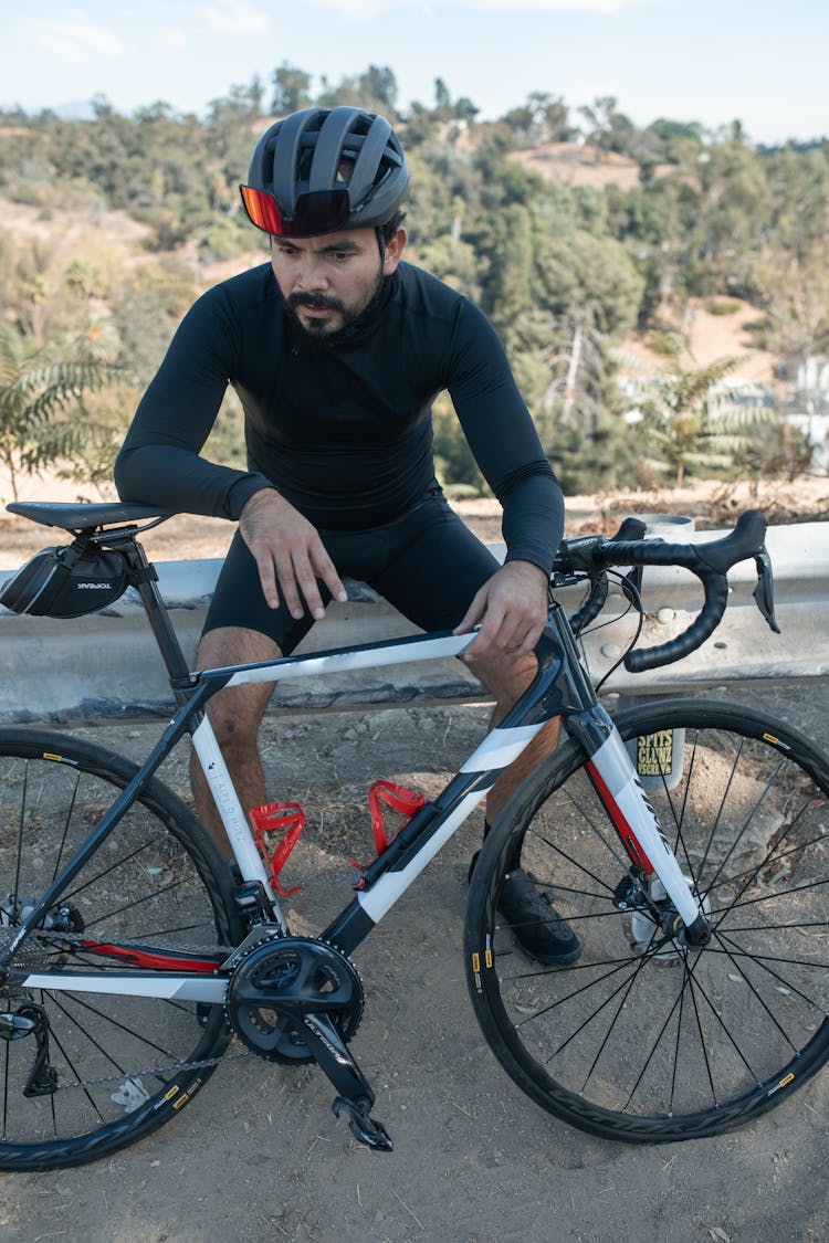 Man Sitting On A Concrete Railing With His Road Bike