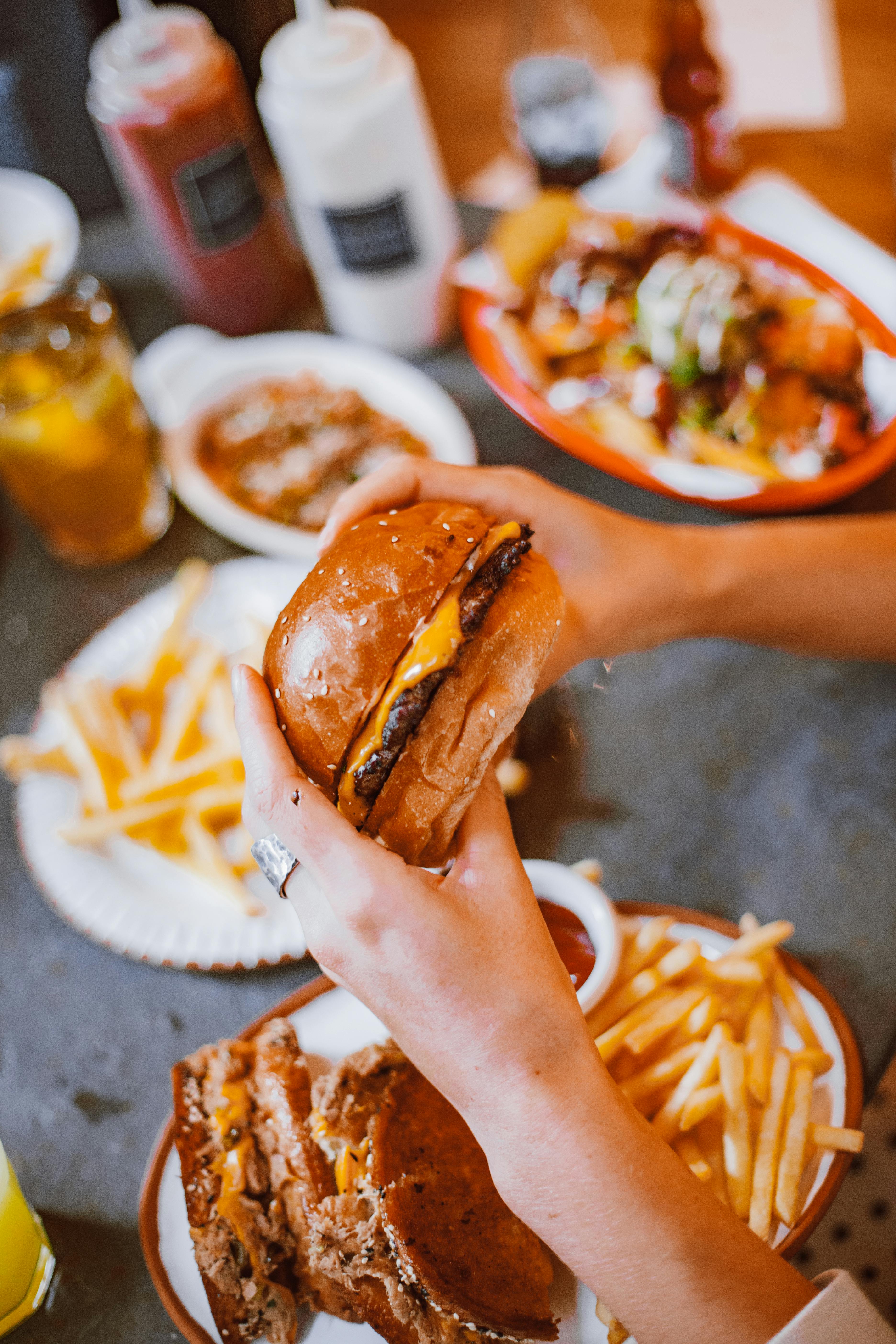 Juicy gourmet burger held above a feast of fries and sides, perfect for fast food lovers.