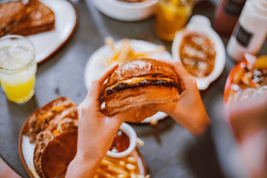 Delicious beef burger with cheese in hand, surrounded by fries and drinks.