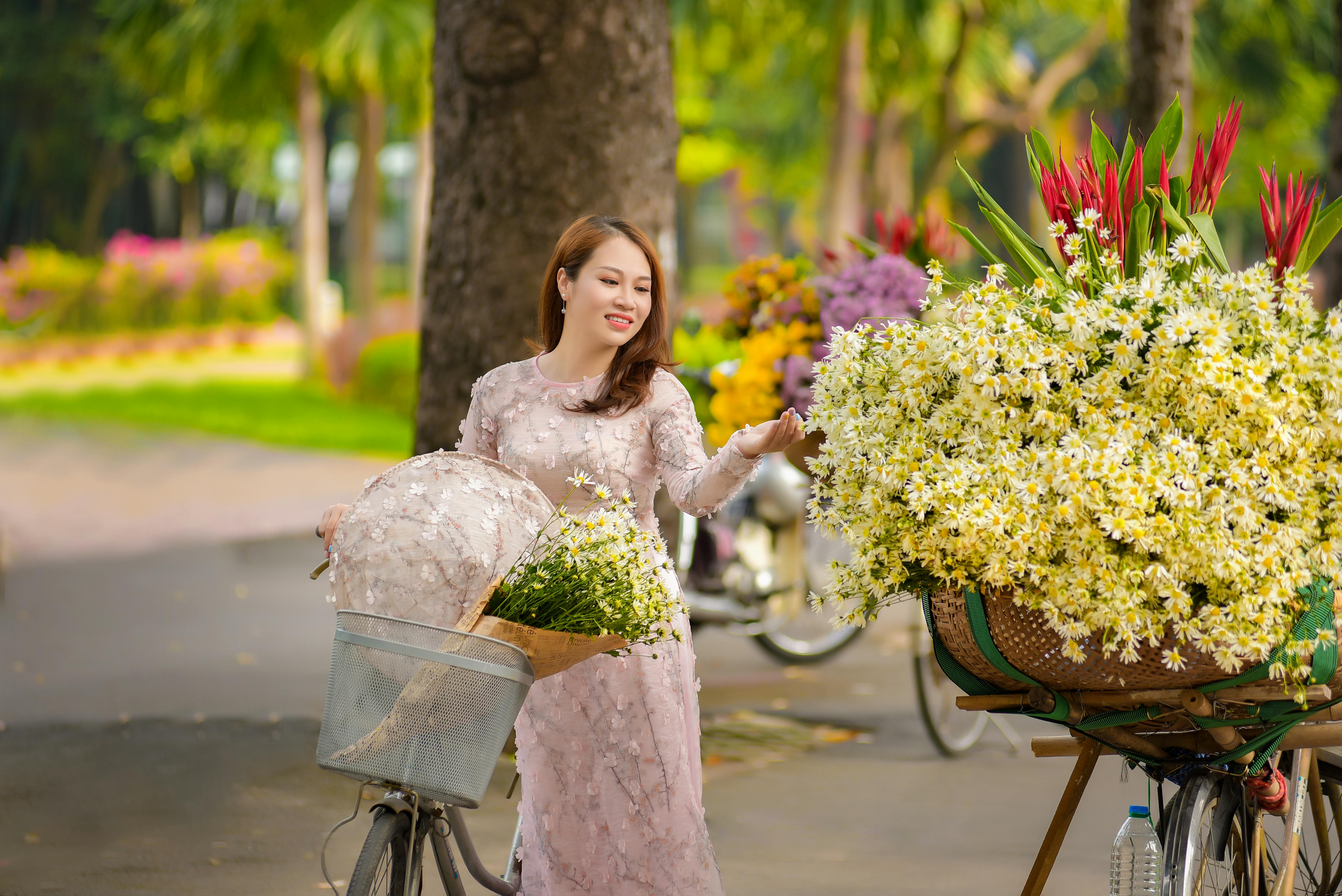 Asian woman in fashionable dress with bicycles and flowers in a park setting.
