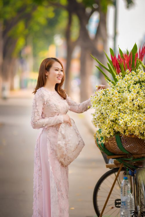 Free Elegant asian woman in ao dai posing with a vibrant bicycle cart of flowers on a sunny day. Stock Photo