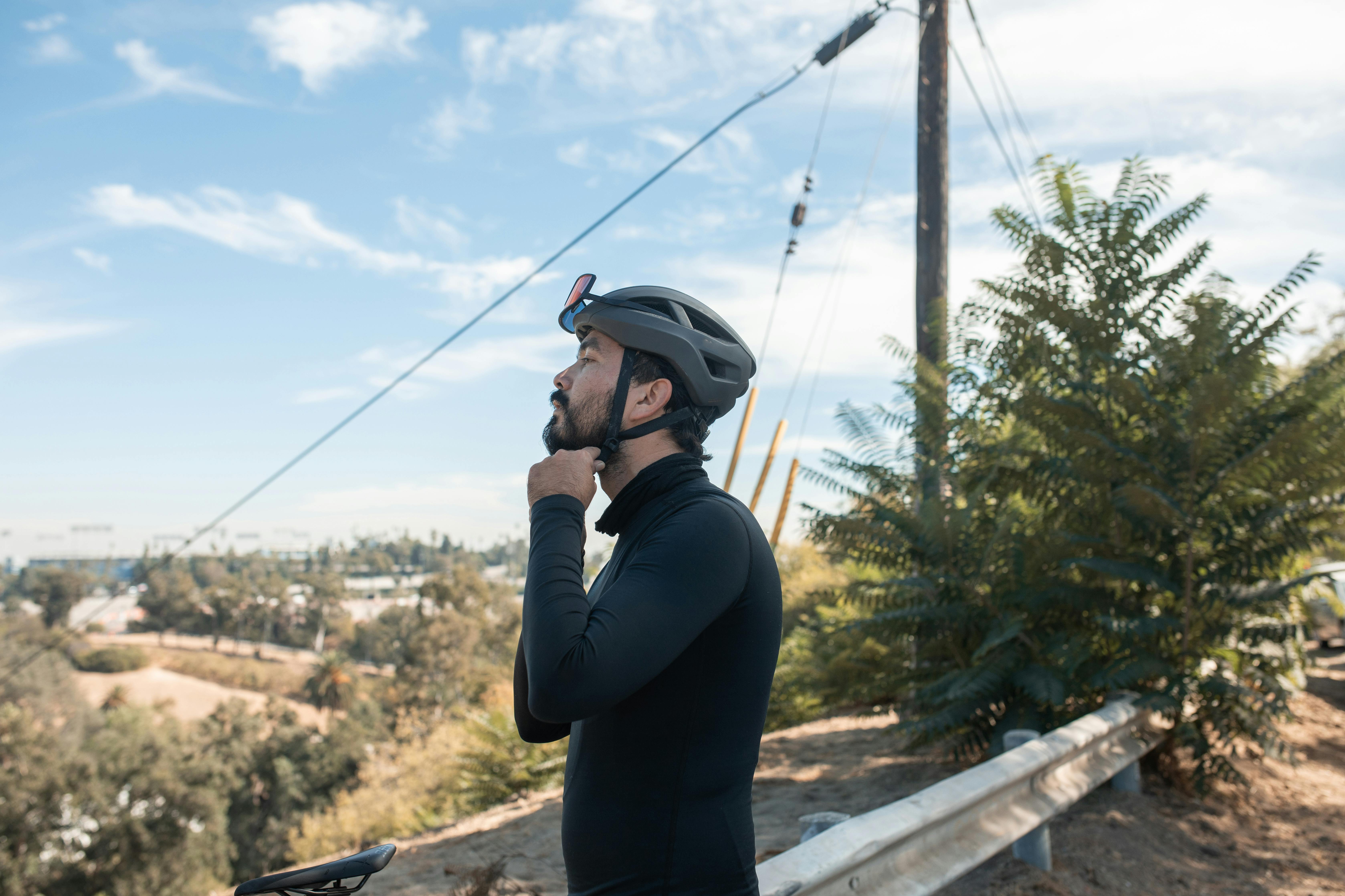 Free Man adjusting helmet before cycling on a sunny day. Outdoor exercise and safety preparation. Stock Photo