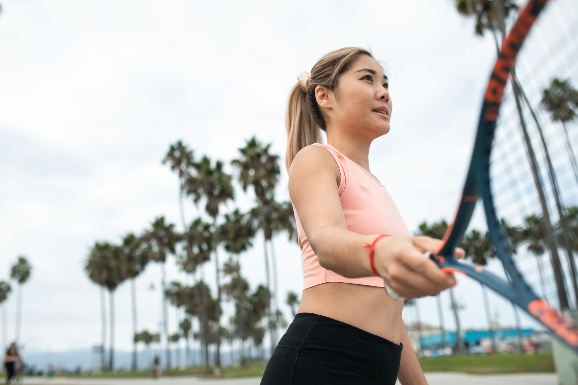 A woman in activewear playing tennis outdoors on a sunny day.